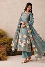 Woman wearing a greyish blue salwar suit in shimmer silk with floral thread embroidery, santoon pant and chiffon dupatta, full-length front view.