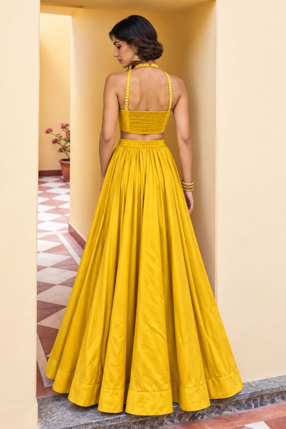 Back view of a mustard yellow lehenga for wedding in roman silk with plain skirt, embroidered halter straps and full flared silhouette.