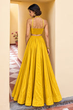 Back view of a mustard yellow lehenga for wedding in roman silk with plain skirt, embroidered halter straps and full flared silhouette.