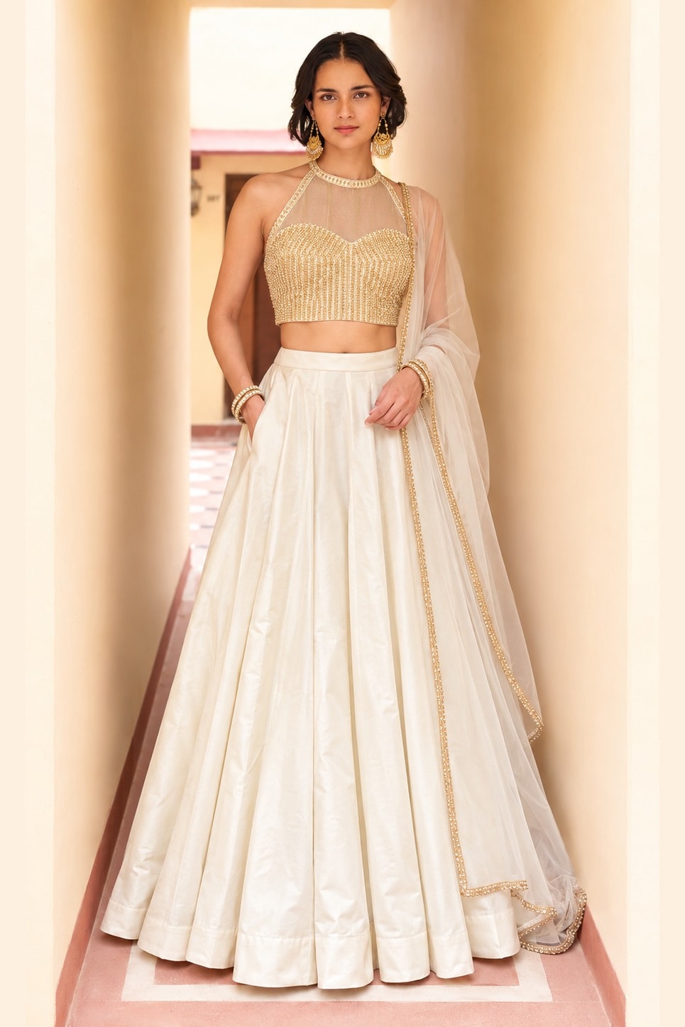 Woman wearing a cream wedding lehenga in roman silk with gold embroidered halter net choli and sheer net dupatta, full-length front view.