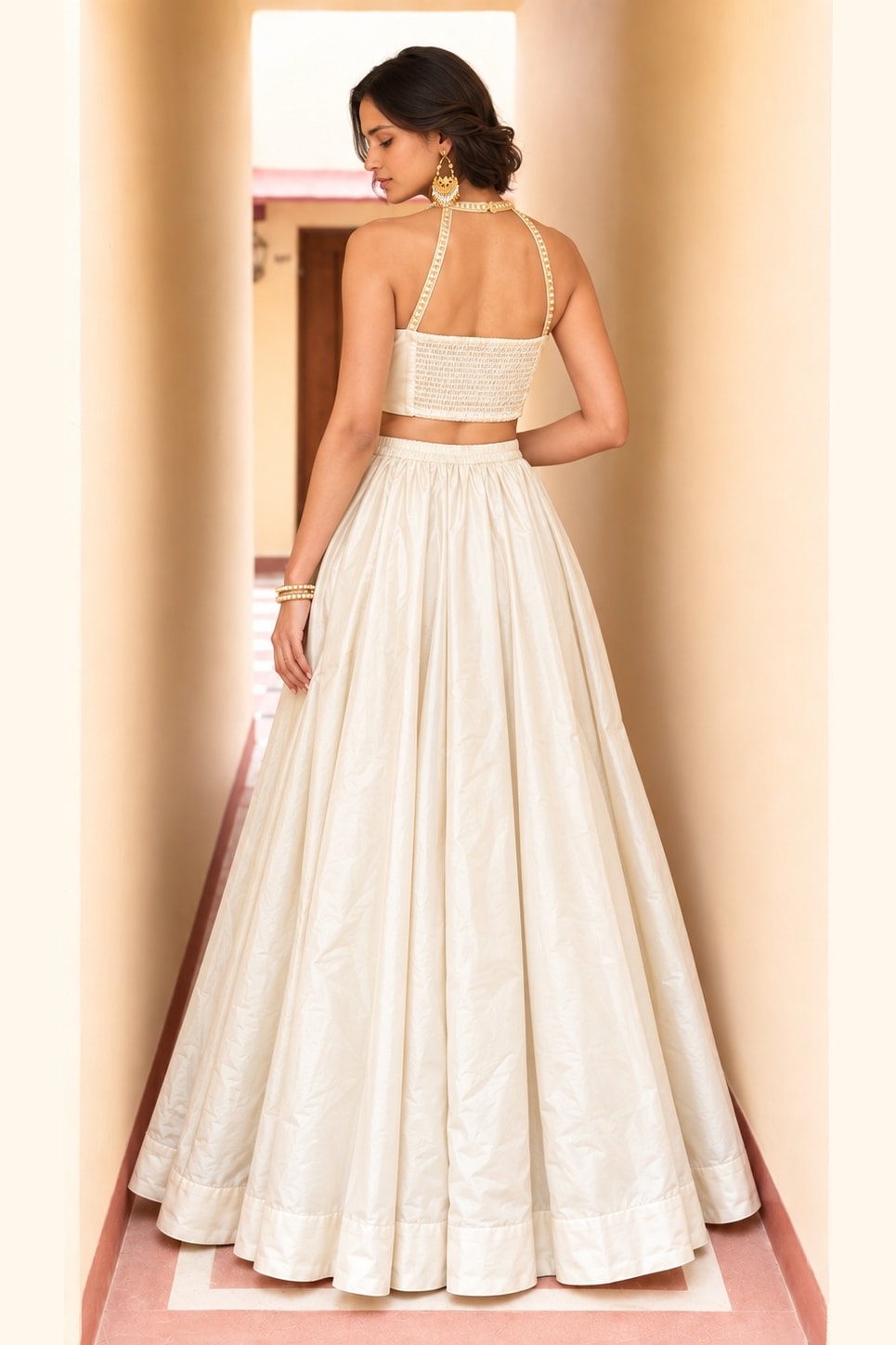 Back view of a cream wedding guest lehenga in roman silk with plain flared skirt and embroidered halter-strap net choli.