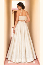 Back view of a cream wedding guest lehenga in roman silk with plain flared skirt and embroidered halter-strap net choli.