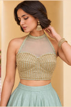 Close-up front view of a pista green lehenga choli for sangeet with heavy embroidery work on the halter neck net choli and jhumka earrings.