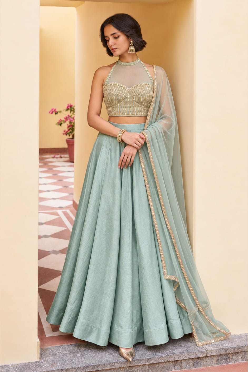 Woman wearing a pista green sequin lehenga in roman silk with embroidered halter net choli and net dupatta, full-length front view.