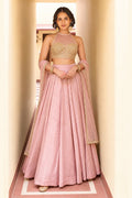 Woman wearing a light pink lehenga for wedding in roman silk with embroidered halter net choli and net dupatta, full-length front view.