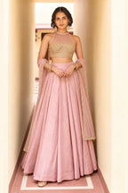Woman wearing a light pink lehenga for wedding in roman silk with embroidered halter net choli and net dupatta, full-length front view.