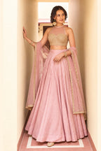 Woman wearing a light pink party lehenga in roman silk with embroidered halter net choli and net dupatta, full-length front view.
