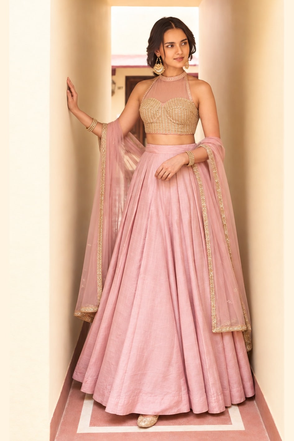 Woman wearing a light pink party lehenga in roman silk with embroidered halter net choli and net dupatta, full-length front view.