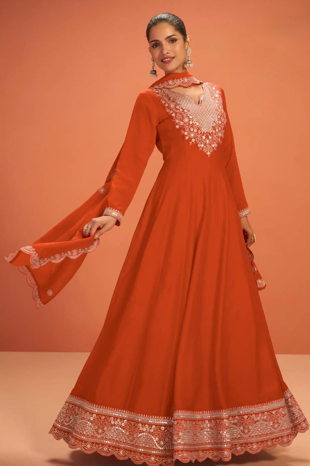 Woman wearing a neon orange wedding anarkali dress in premium silk with sequin and thread embroidery and silk dupatta, full-length front view.