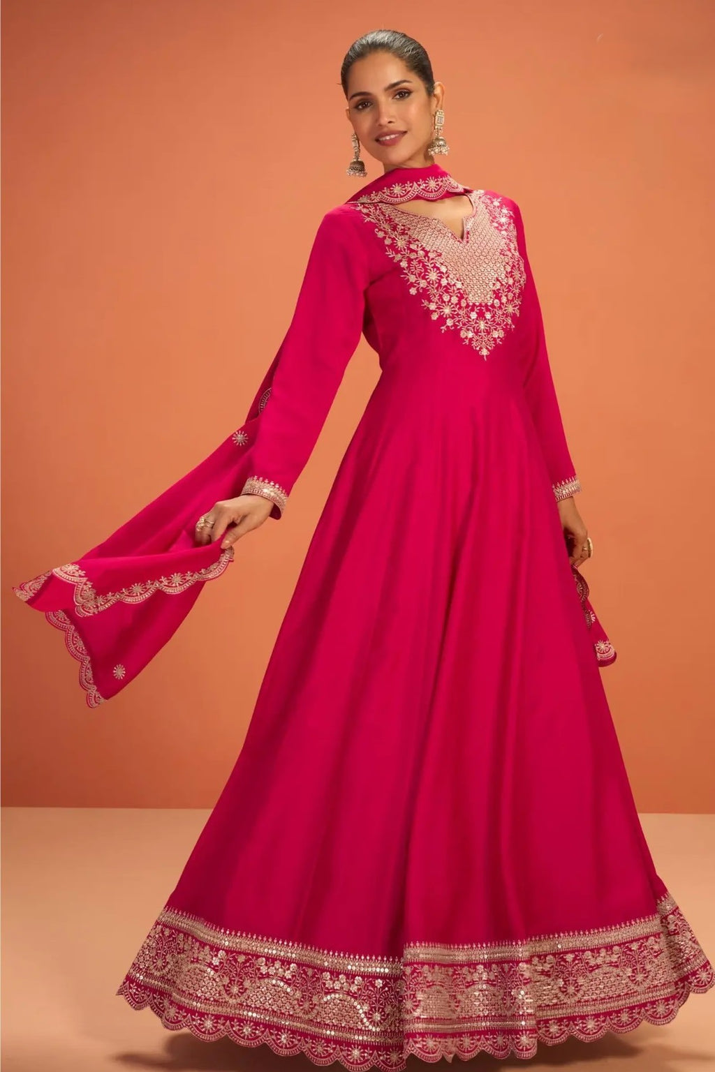 Woman wearing a pinkish red anarkali dress for wedding in premium silk with sequin and thread embroidery and silk dupatta, full-length front view.