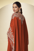 Back close-up view of a rust indian palazzo dresses style outfit showing gold embroidery across the shoulders and long cape sleeves.