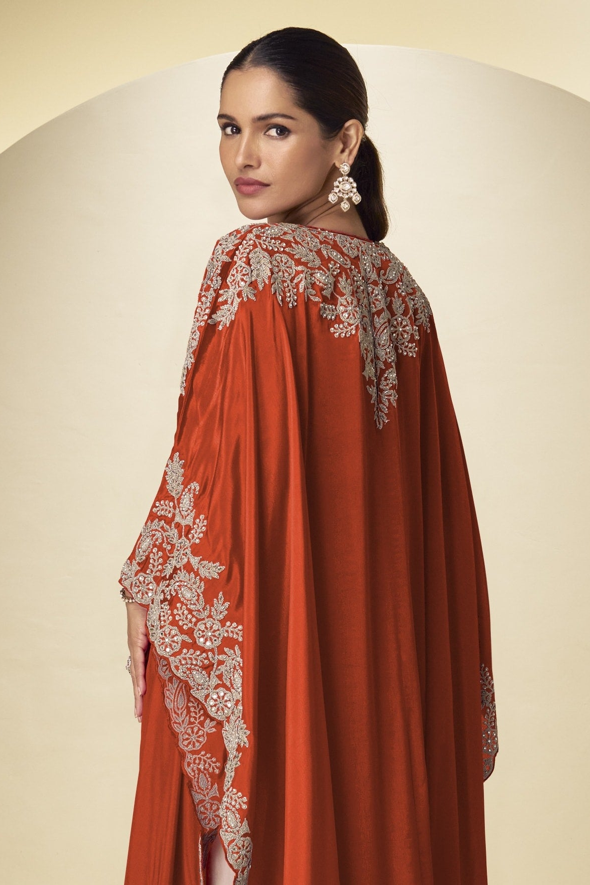 Back close-up view of a rust indian palazzo dresses style outfit showing gold embroidery across the shoulders and long cape sleeves.