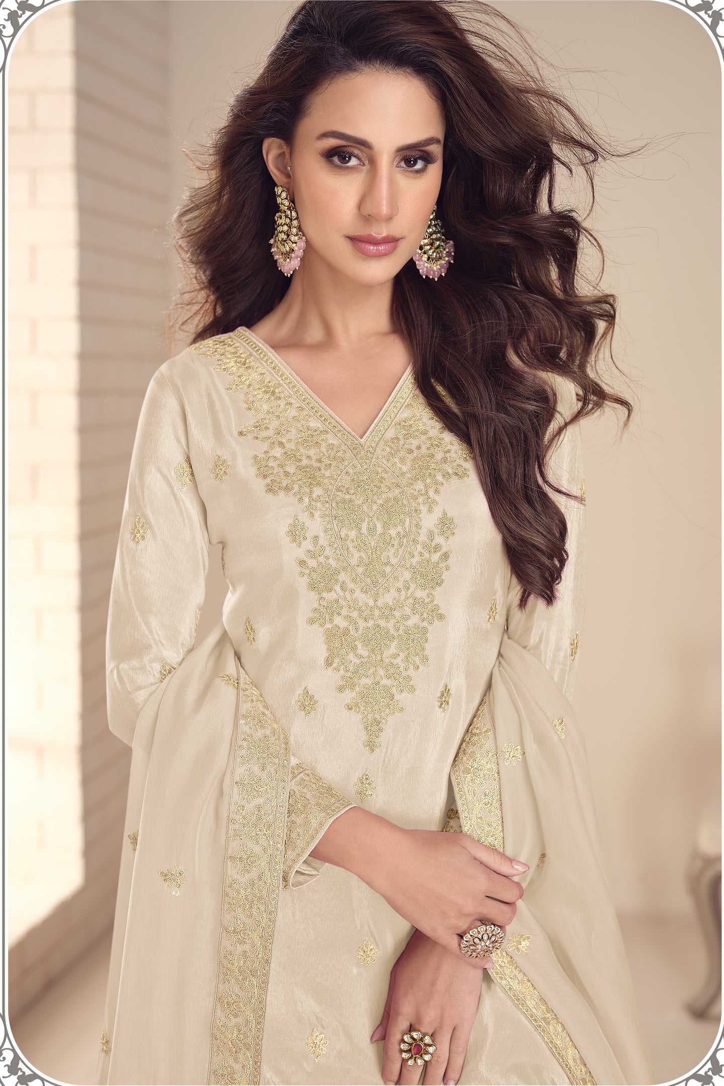 Woman wearing a light-colored dress with intricate designs indoors.