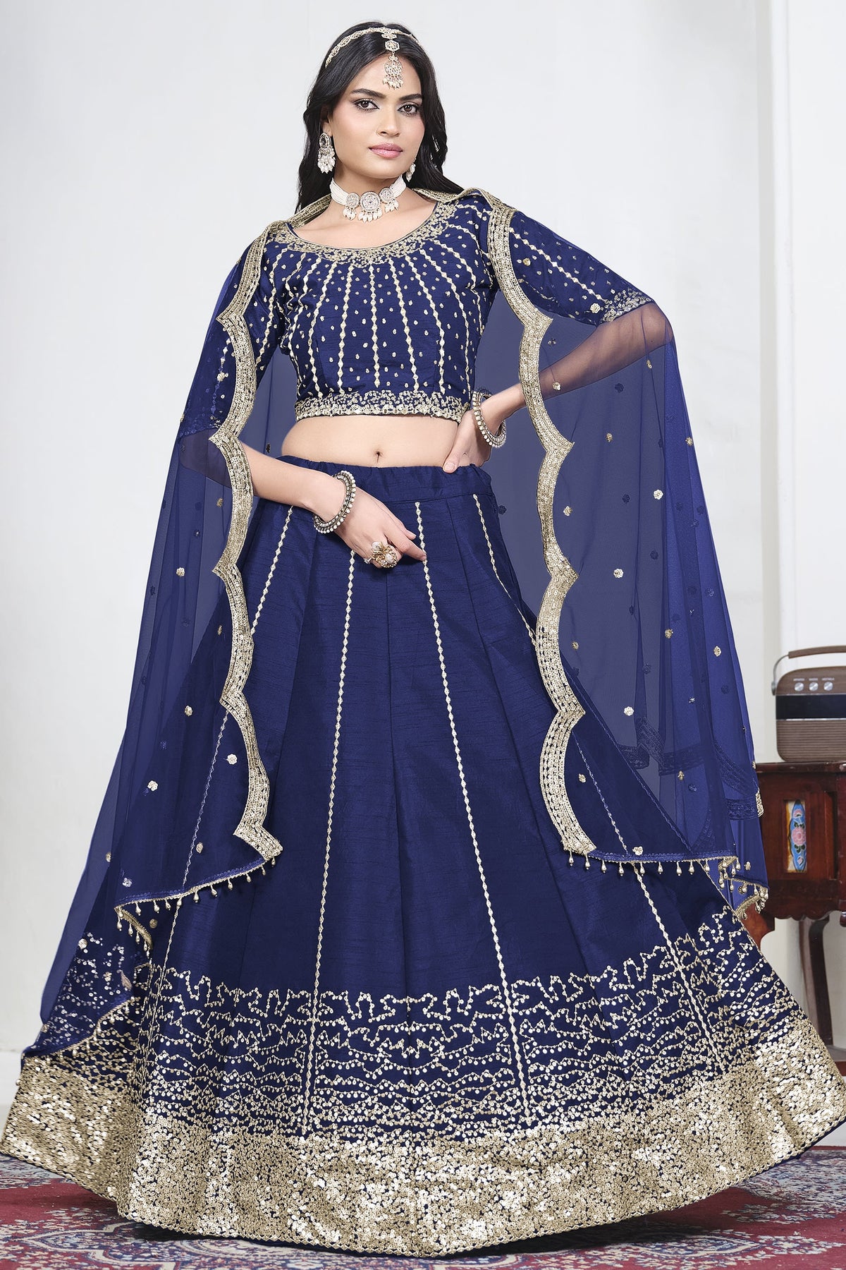 Woman wearing a navy blue lehenga skirt with mirror work, half sleeve round neck art silk choli, full-length front view.