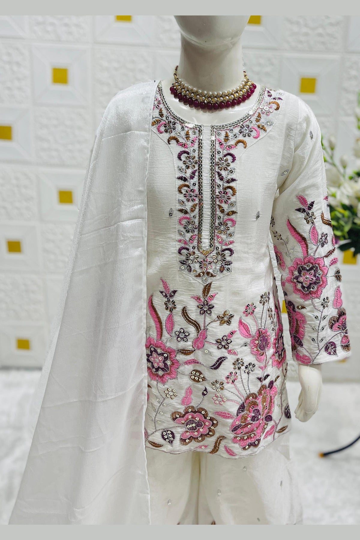 Close-up of off white childrens indian outfit, pink floral sequins and thread work detail on chinon silk fabric.