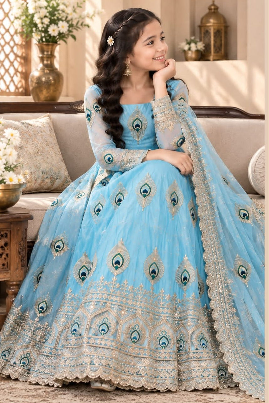 Girl in a sky blue indian kidswear anarkali set seated on a sofa, full embroidered gown and dupatta visible in the photo.