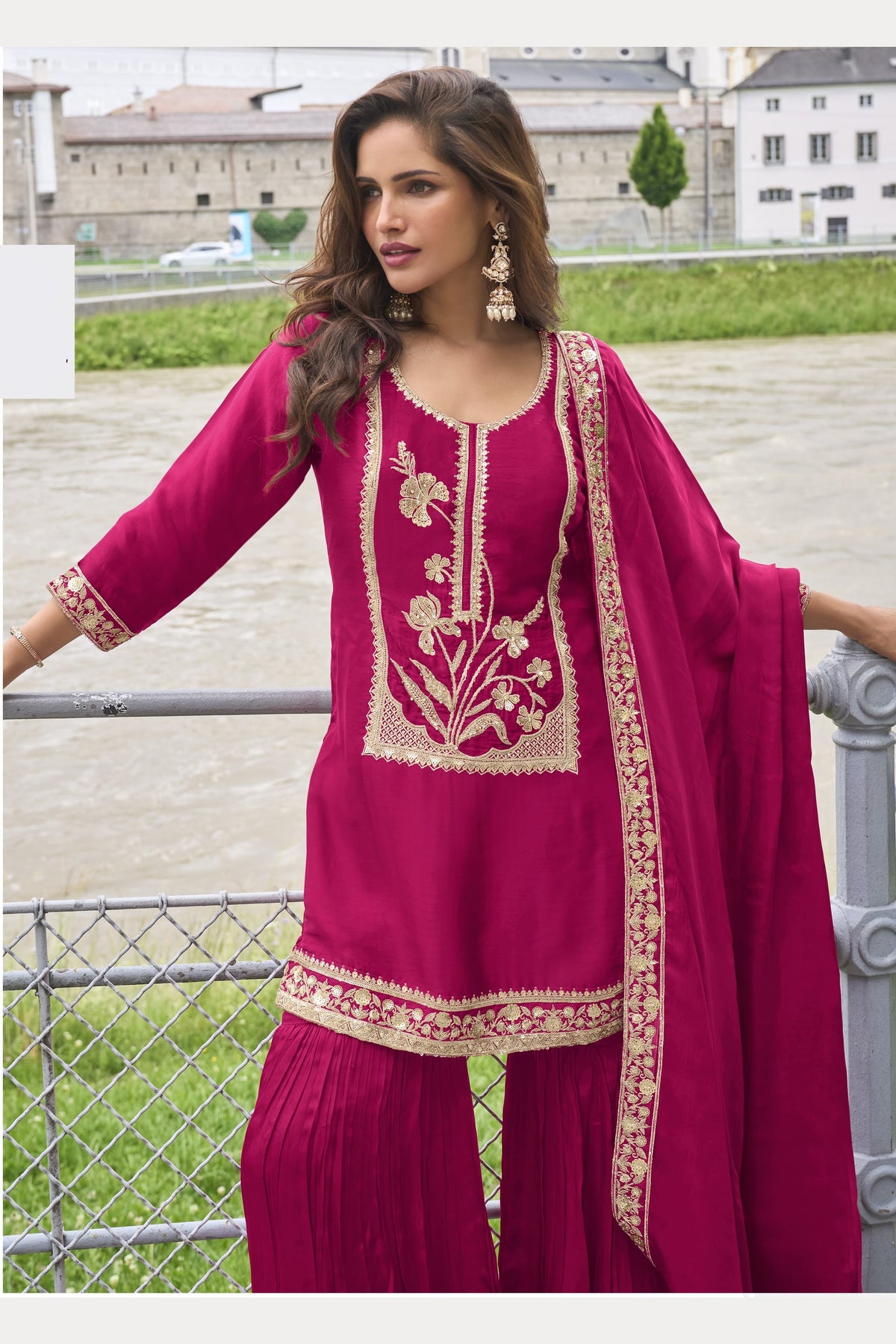 Model wearing a Reddish Pink sharara suit with embroidered pure silk kurta and dupatta, full-length side view.