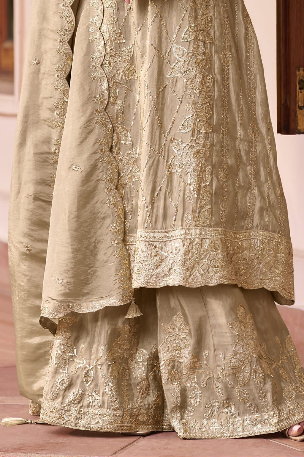 lower view of Model wearing a beige palazzo suit with scalloped simmer silk dupatta, showing the hand-embroidered kurta and wide plazo pants in full length.