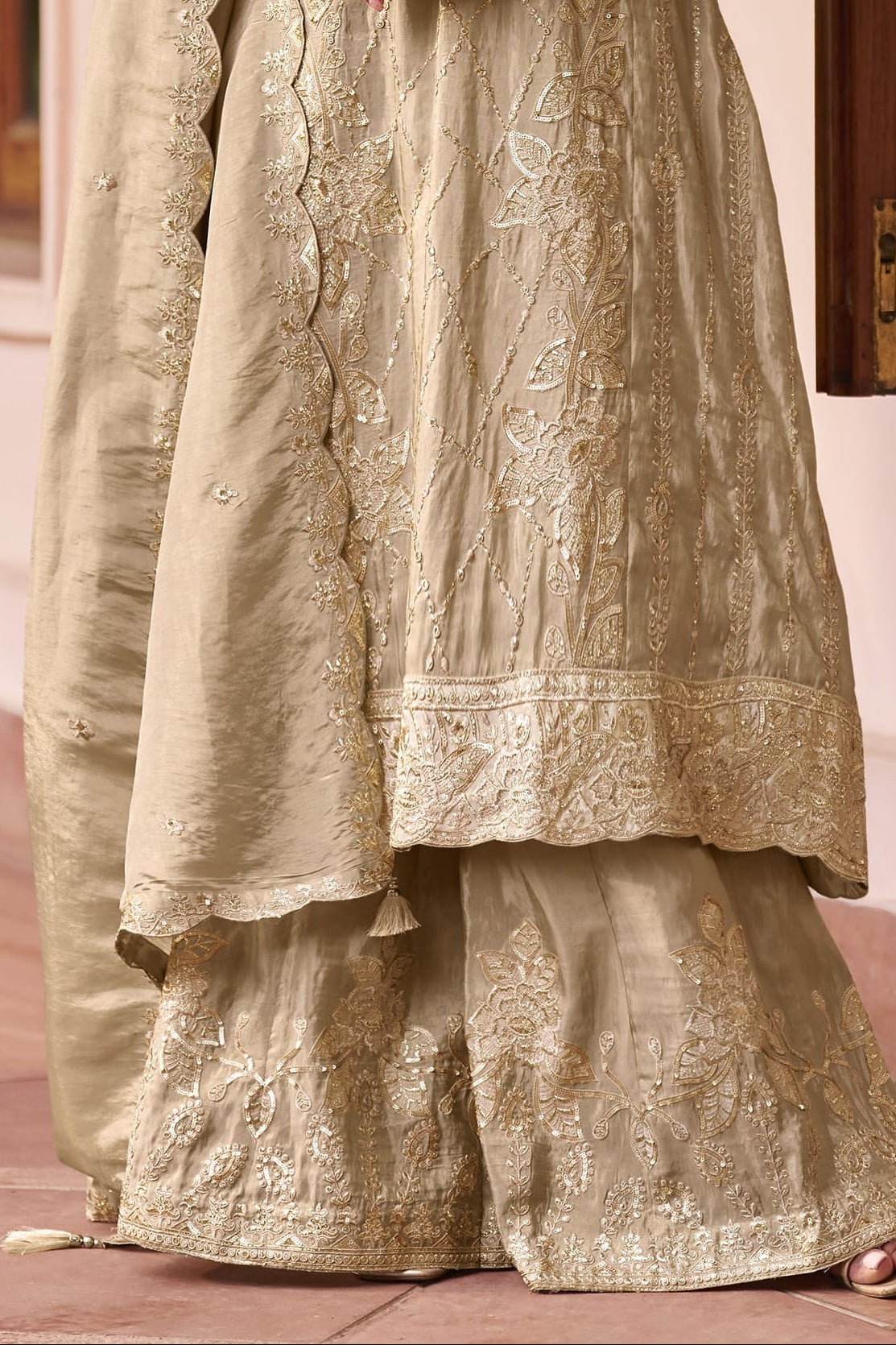 lower view of Model wearing a beige palazzo suit with scalloped simmer silk dupatta, showing the hand-embroidered kurta and wide plazo pants in full length.