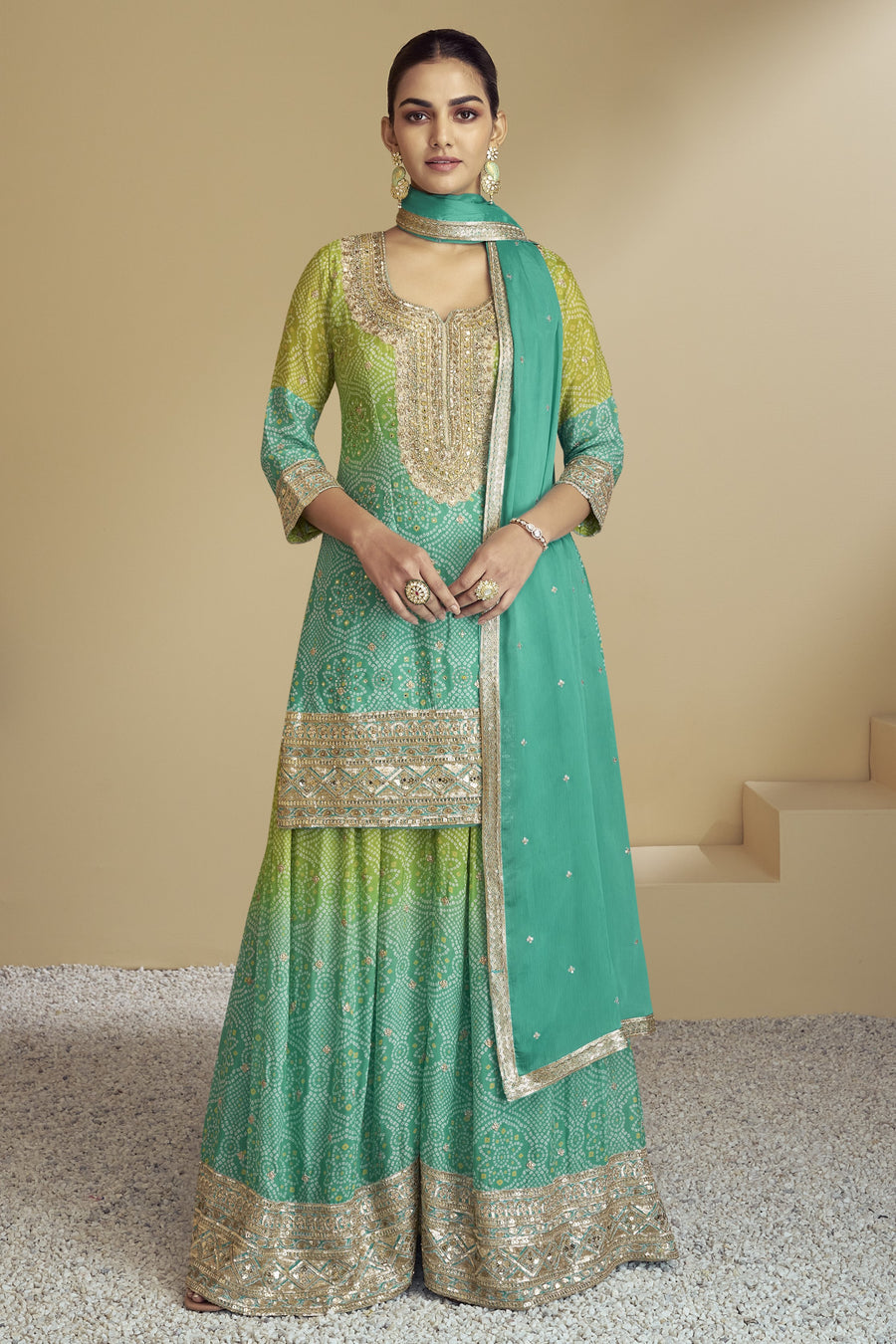 A woman wearing a green and beige chinon silk bandhani style palazzo suit with embroidery work and a dupatta.