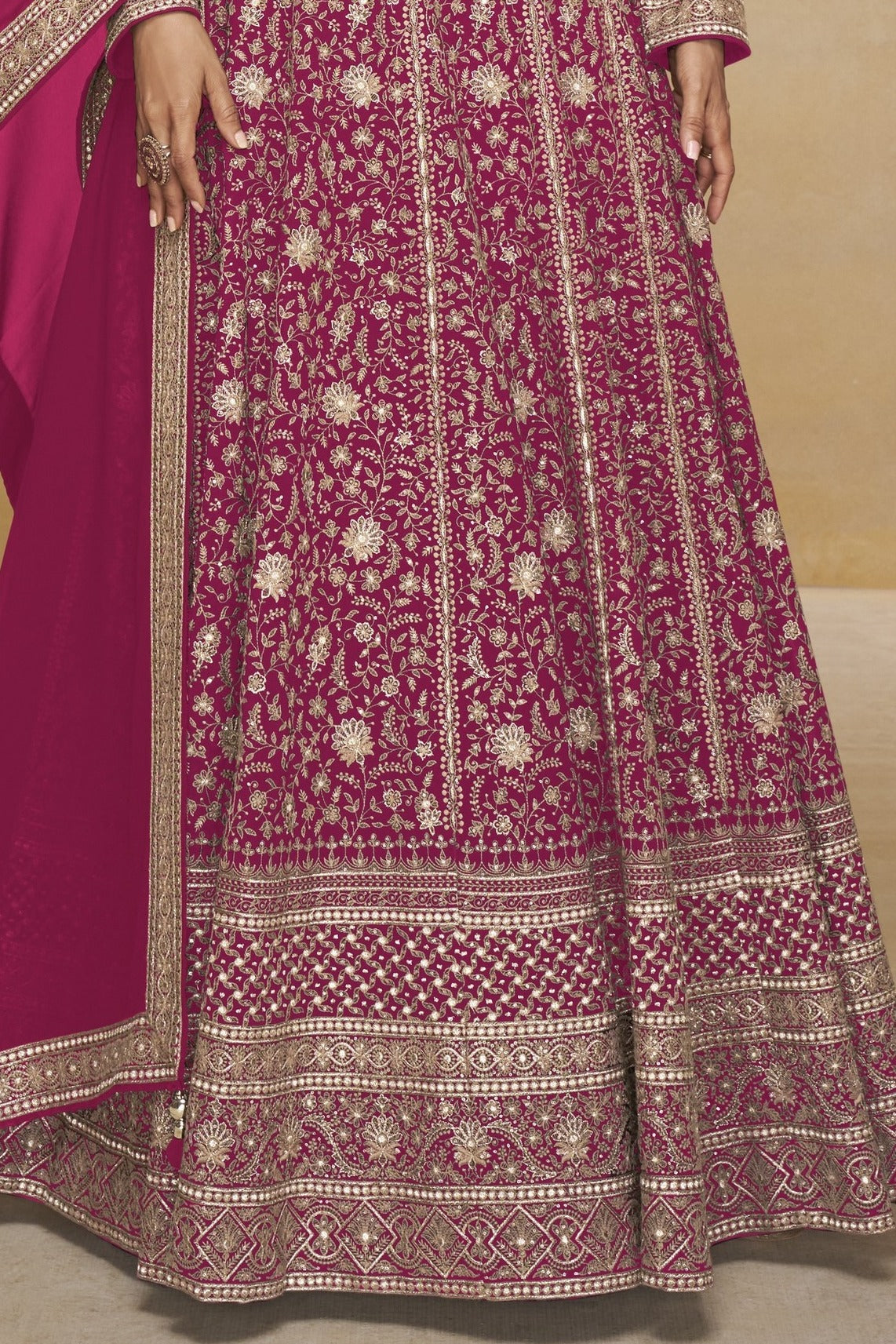 Waist-to-hem view of a dark pink pakistani anarkali suit in georgette with gold zari floral embroidery and wide embroidered border.