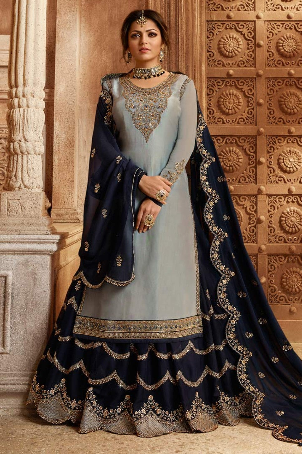 A full front view of a woman wearing a light gray satin georgette wedding kameez with embroidered neckline and navy skirt with gold tiers.