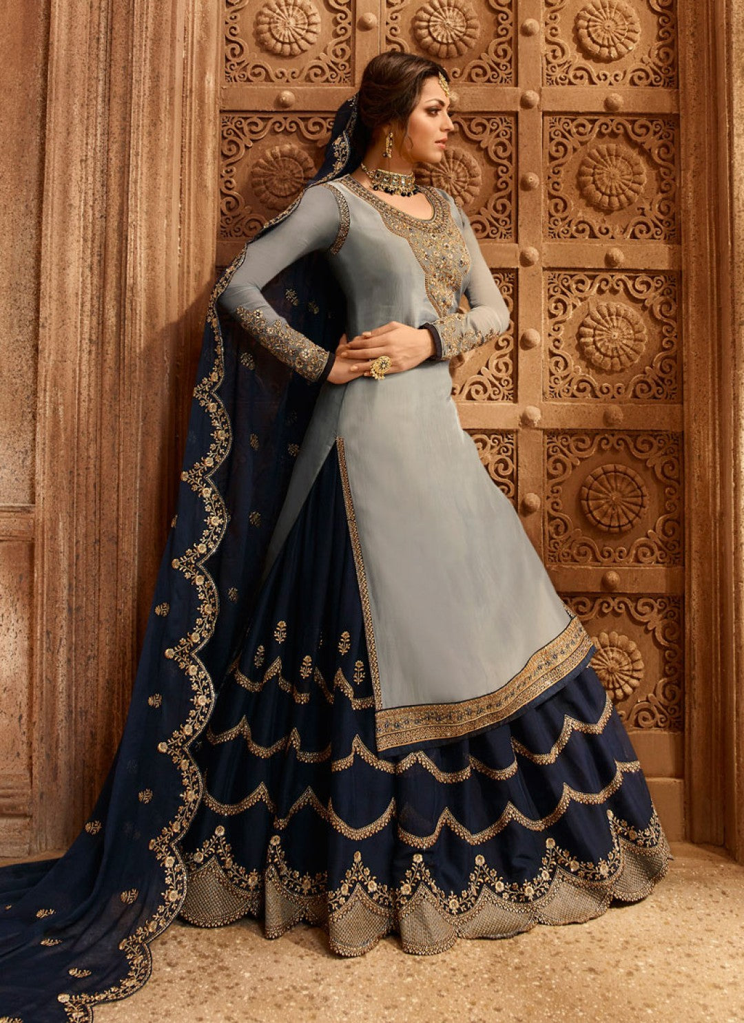A side full view of a woman wearing a light gray kameez for women with a navy embroidered skirt and dupatta over her shoulder.