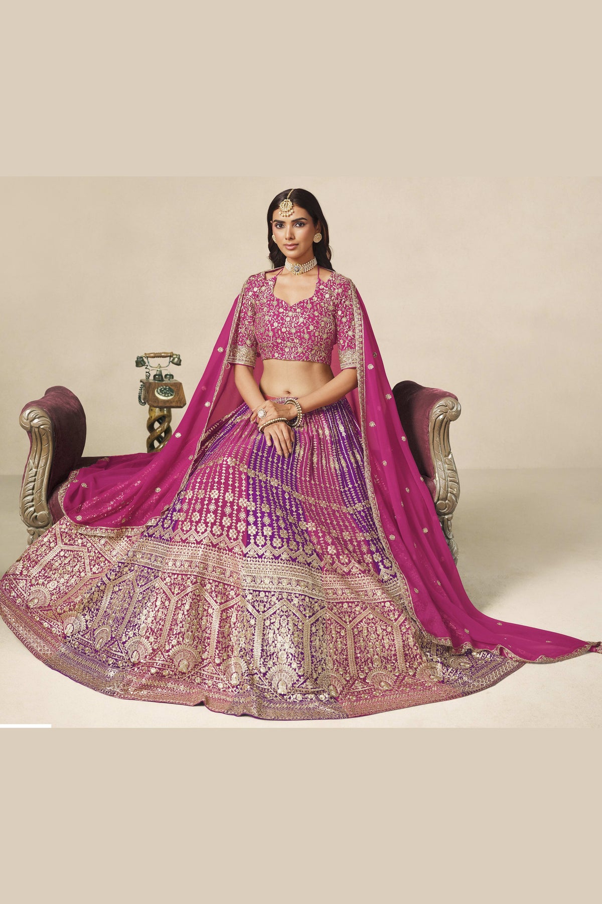 Full-length seated view of a magenta indian wedding guest dresses style lehenga in georgette with zari and sequin work on the flared skirt.