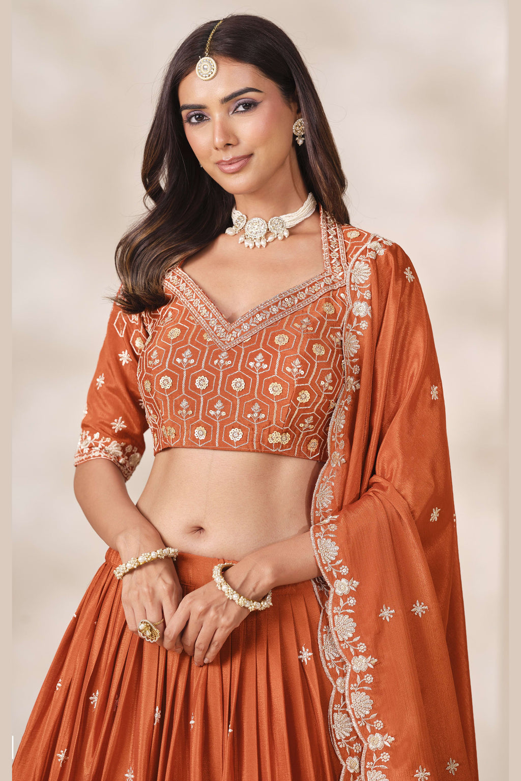 Close-up of a rust orange engagement lehenga blouse in chinon silk with sequin and thread embroidery on the V neckline and elbow sleeves.