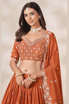 Close-up of a rust orange engagement lehenga blouse in chinon silk with sequin and thread embroidery on the V neckline and elbow sleeves.