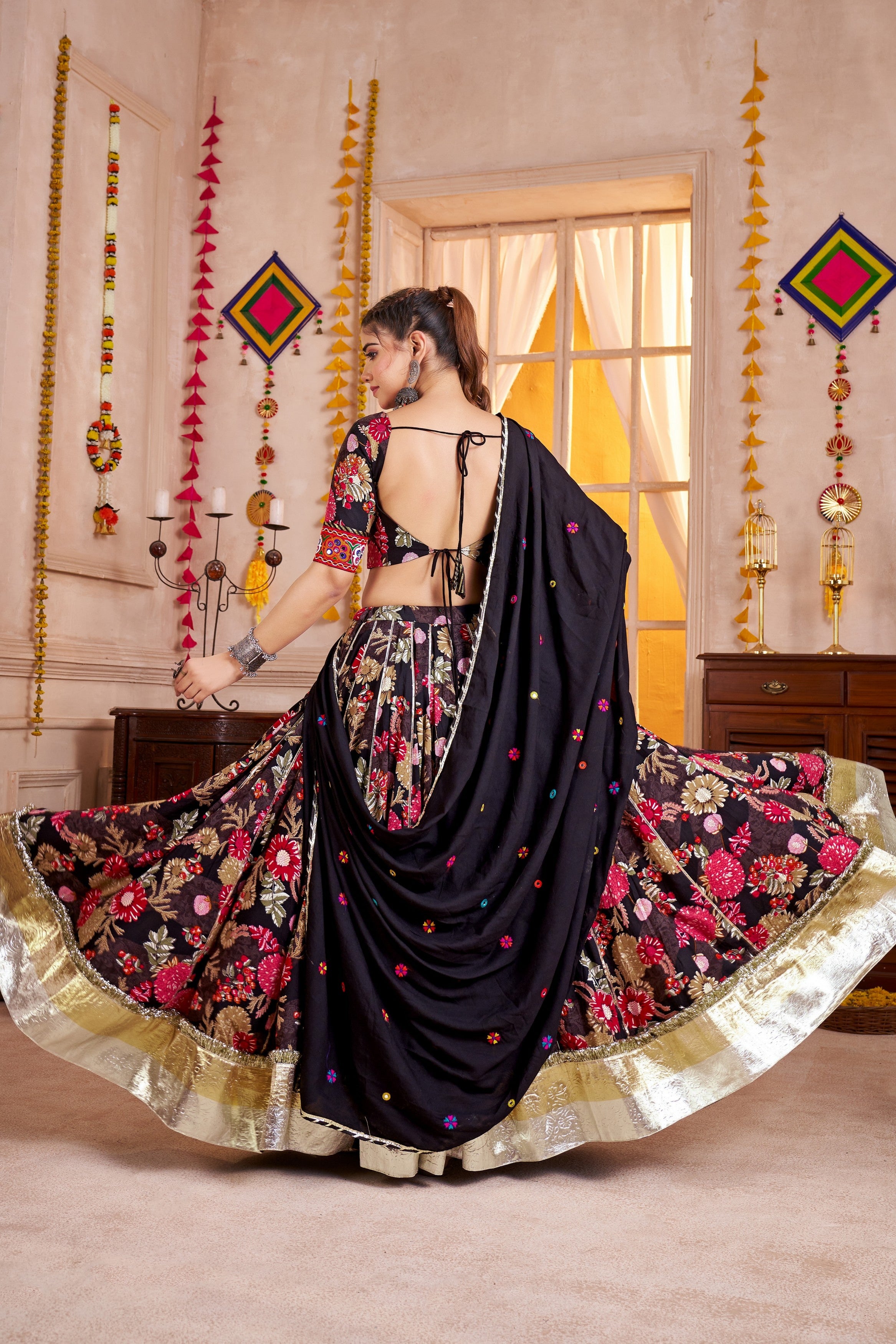 Woman in a traditional black and floral lehenga in a decorated room.