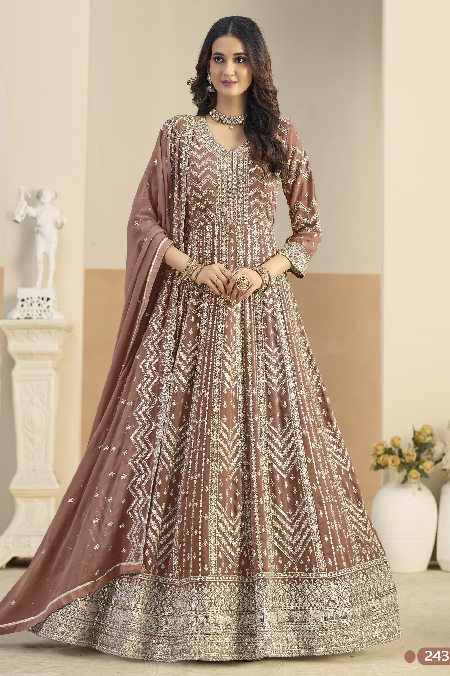 Woman wearing a traditional brown and beige embroidered dress in an indoor setting.