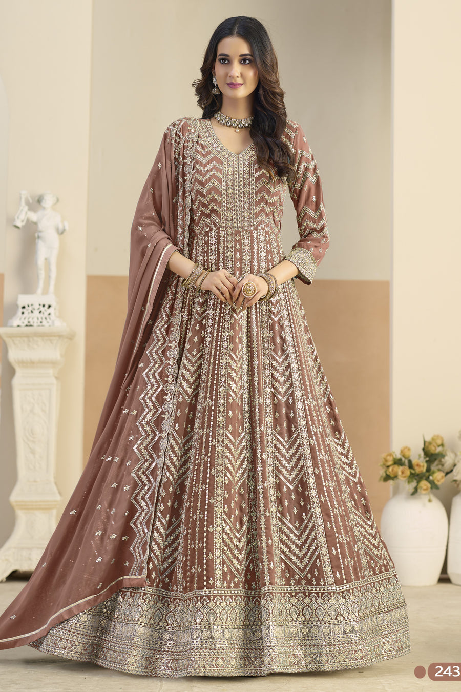 Woman wearing a traditional brown and beige embroidered dress in an indoor setting.