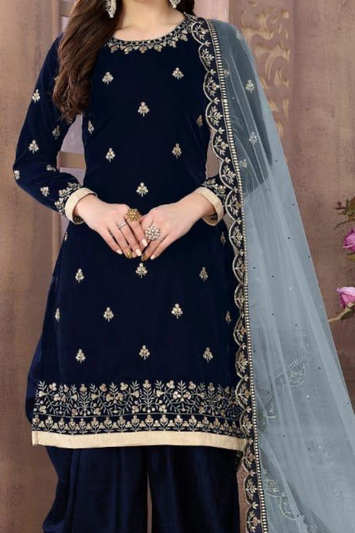 A close-up side detail view of a navy blue outfit from the punjabi female suits range, with an embroidered velvet kameez, hem band and grey net dupatta.