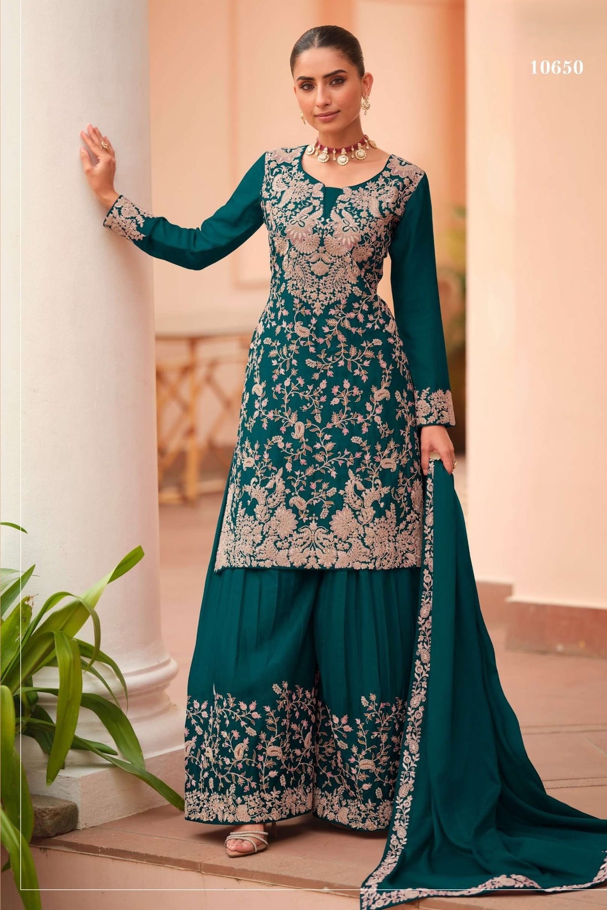 Woman wearing a teal palazzo suit in chinon silk with thread embroidery work, paired with an embroidered plazo and dupatta, full-length front view.