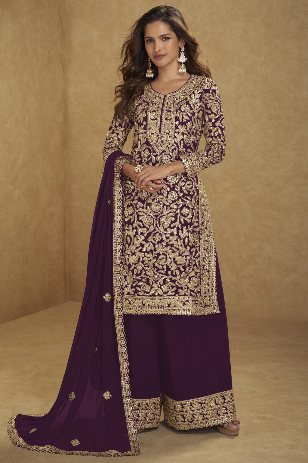 Woman wearing a traditional embroidered outfit with a purple dupatta against a beige background