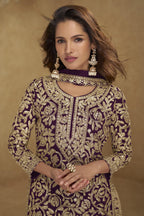 Woman wearing a purple and gold embroidered traditional outfit with jewelry against a brown background