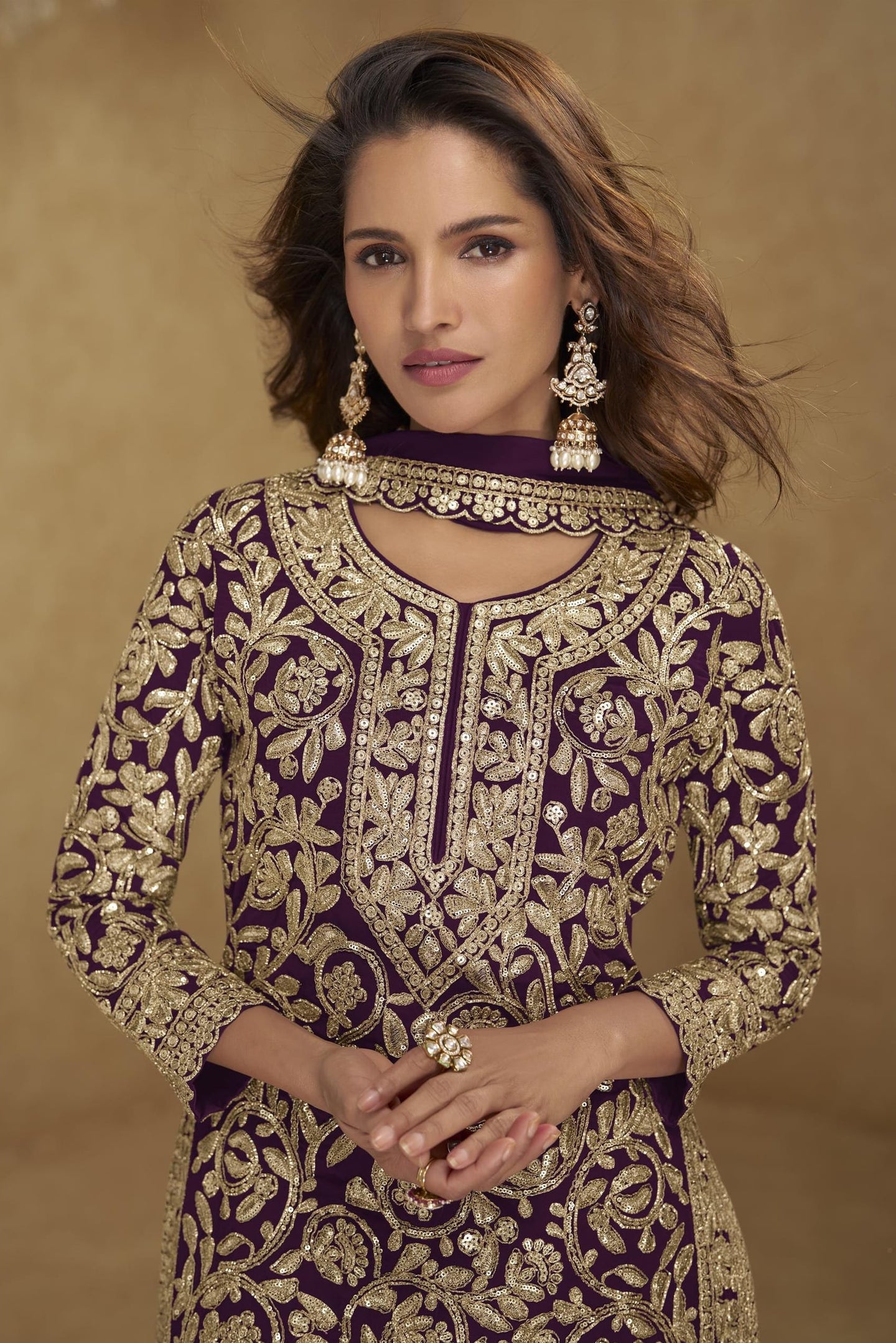 Woman wearing a purple and gold embroidered traditional outfit with jewelry against a brown background