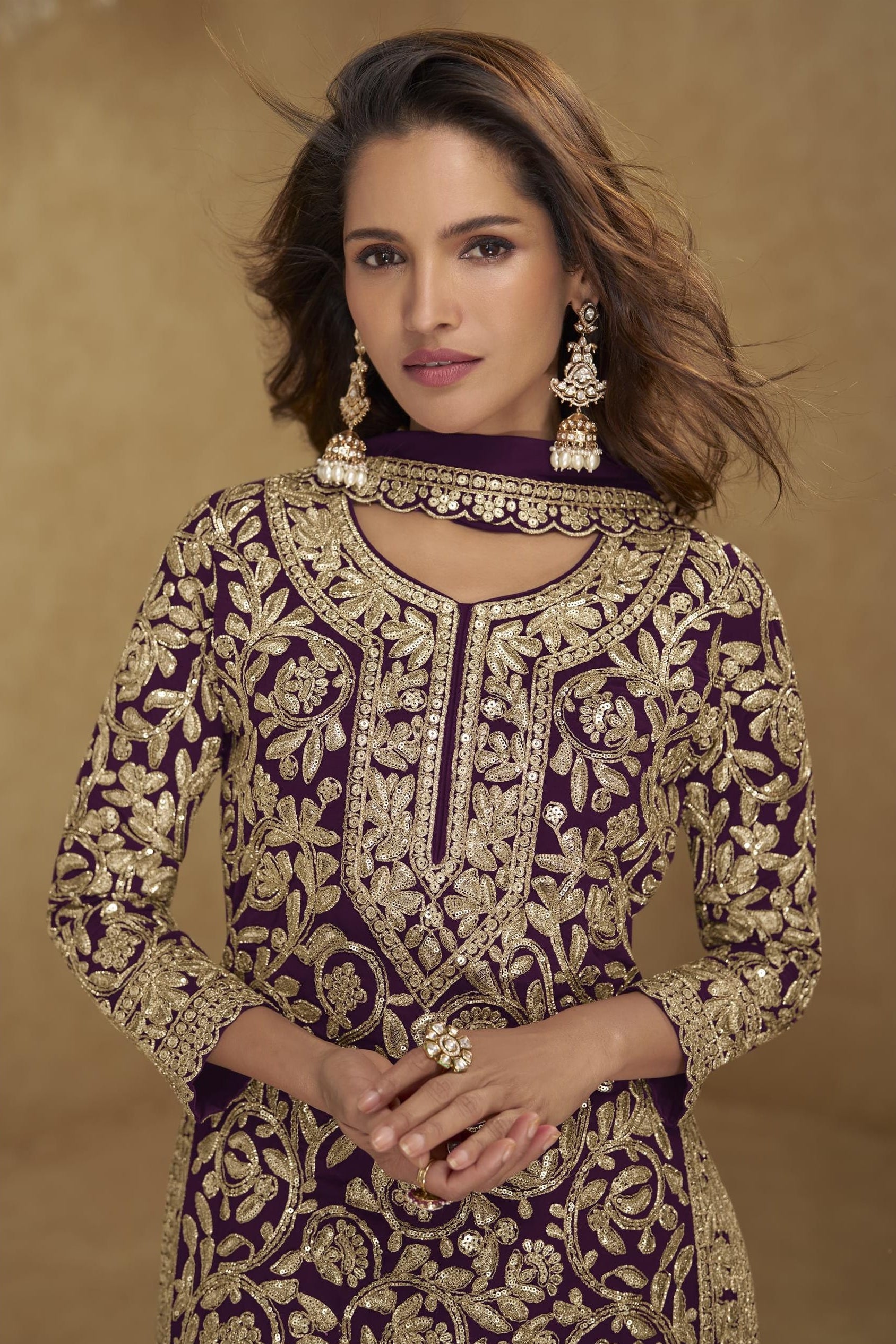 Woman wearing a purple and gold embroidered traditional outfit with jewelry against a brown background