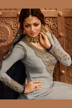 A waist-up view of a woman with looking slant wearing a light gray kameez suit with a gold embroidered neckline, embroidered cuffs and a dupatta border.