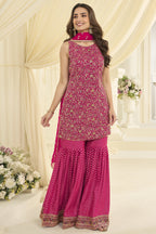 Woman wearing a reddish pink gharara suit in georgette with Swarovski, Zarkan and embroidery work, paired with a woven jacquard gharara, full-length front view.