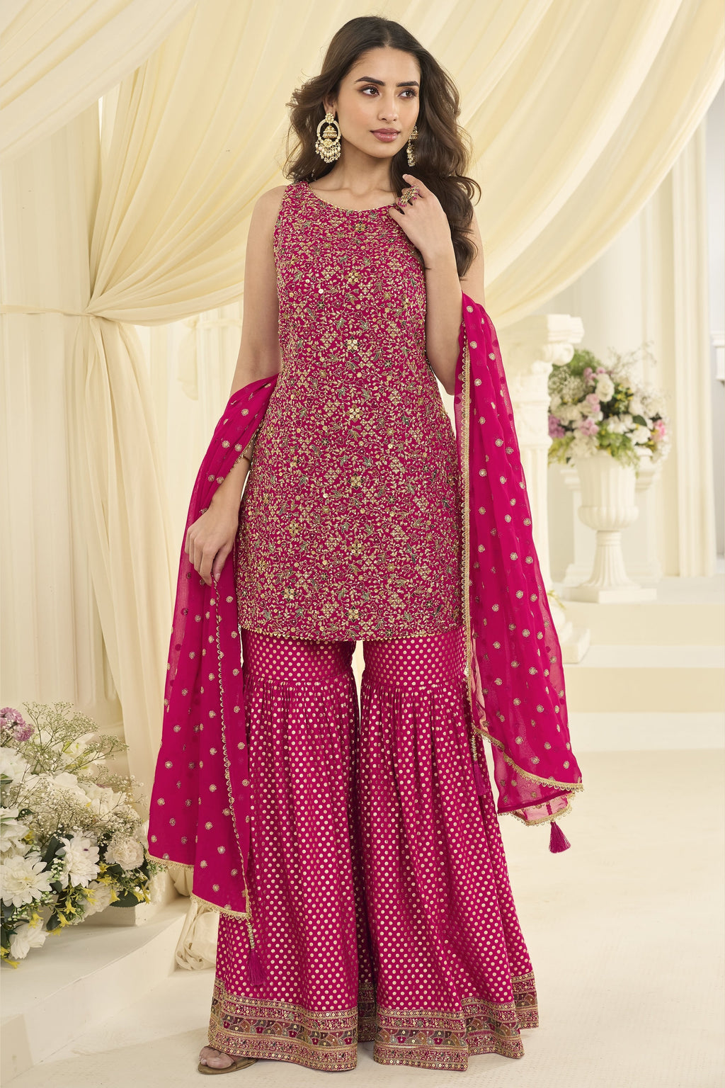 Full-length side view of a reddish pink wedding gharara suit in georgette with Swarovski, Zarkan and embroidery work, dupatta draped.