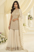 Woman wearing a cream pakistani gharara suit in georgette with Swarovski, Zarkan and embroidery work, paired with a woven jacquard gharara, full-length front view.