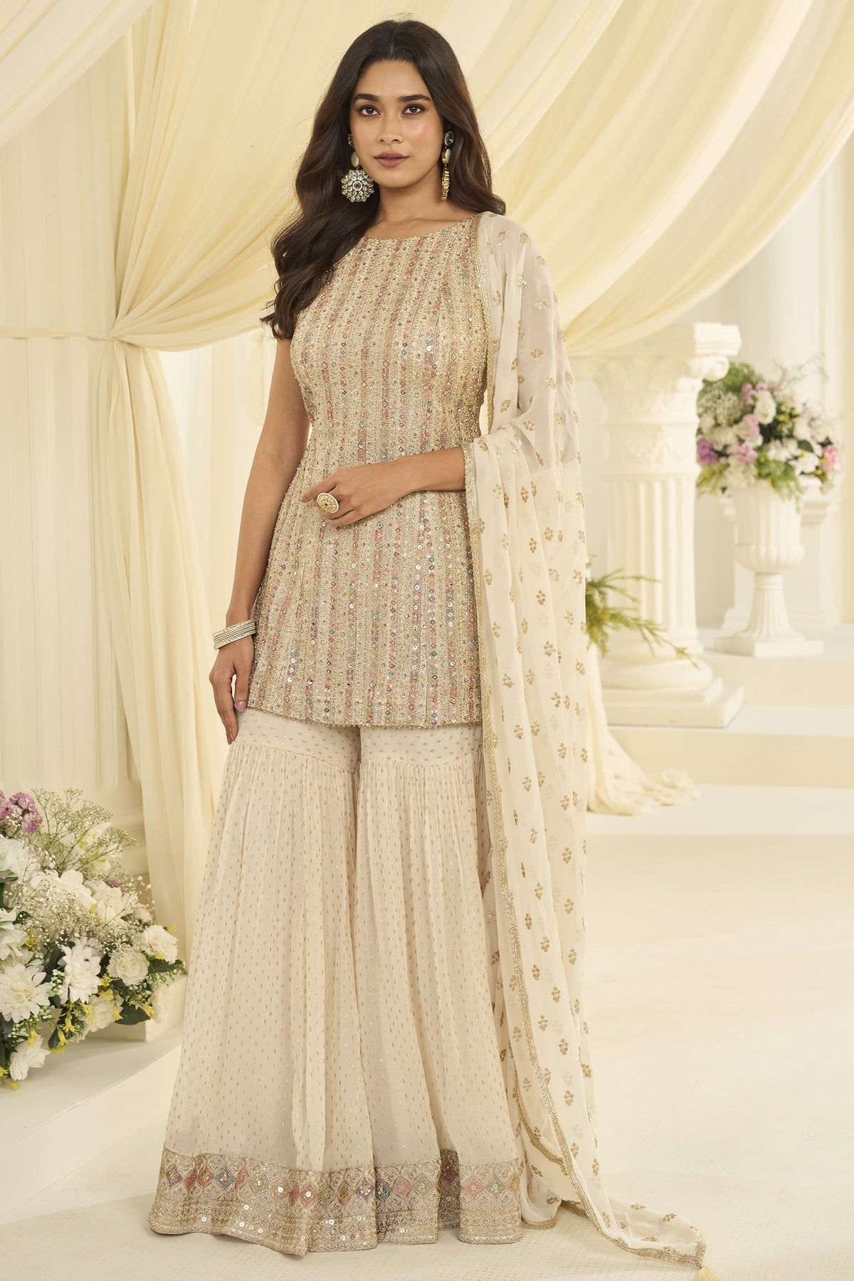 Woman wearing a cream pakistani gharara suit in georgette with Swarovski, Zarkan and embroidery work, paired with a woven jacquard gharara, full-length front view.
