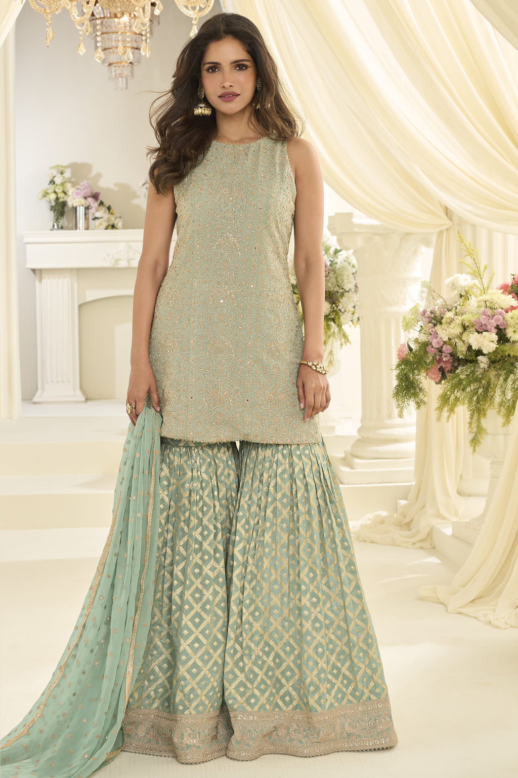 Woman wearing a mint green gharara dress in georgette with Swarovski, Zarkan and embroidery work, paired with a woven jacquard gharara, full-length front view.