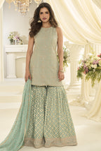Woman wearing a mint green gharara dress in georgette with Swarovski, Zarkan and embroidery work, paired with a woven jacquard gharara, full-length front view.