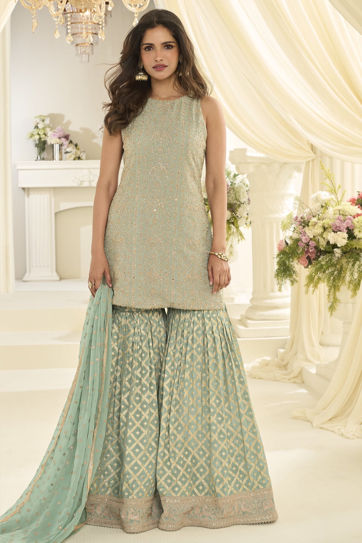 Woman wearing a mint green gharara dress in georgette with Swarovski, Zarkan and embroidery work, paired with a woven jacquard gharara, full-length front view.