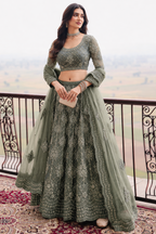 Woman wearing a sage green lehenga for wedding reception with embroidery work, three quarter sleeve round neck net choli, full front view.