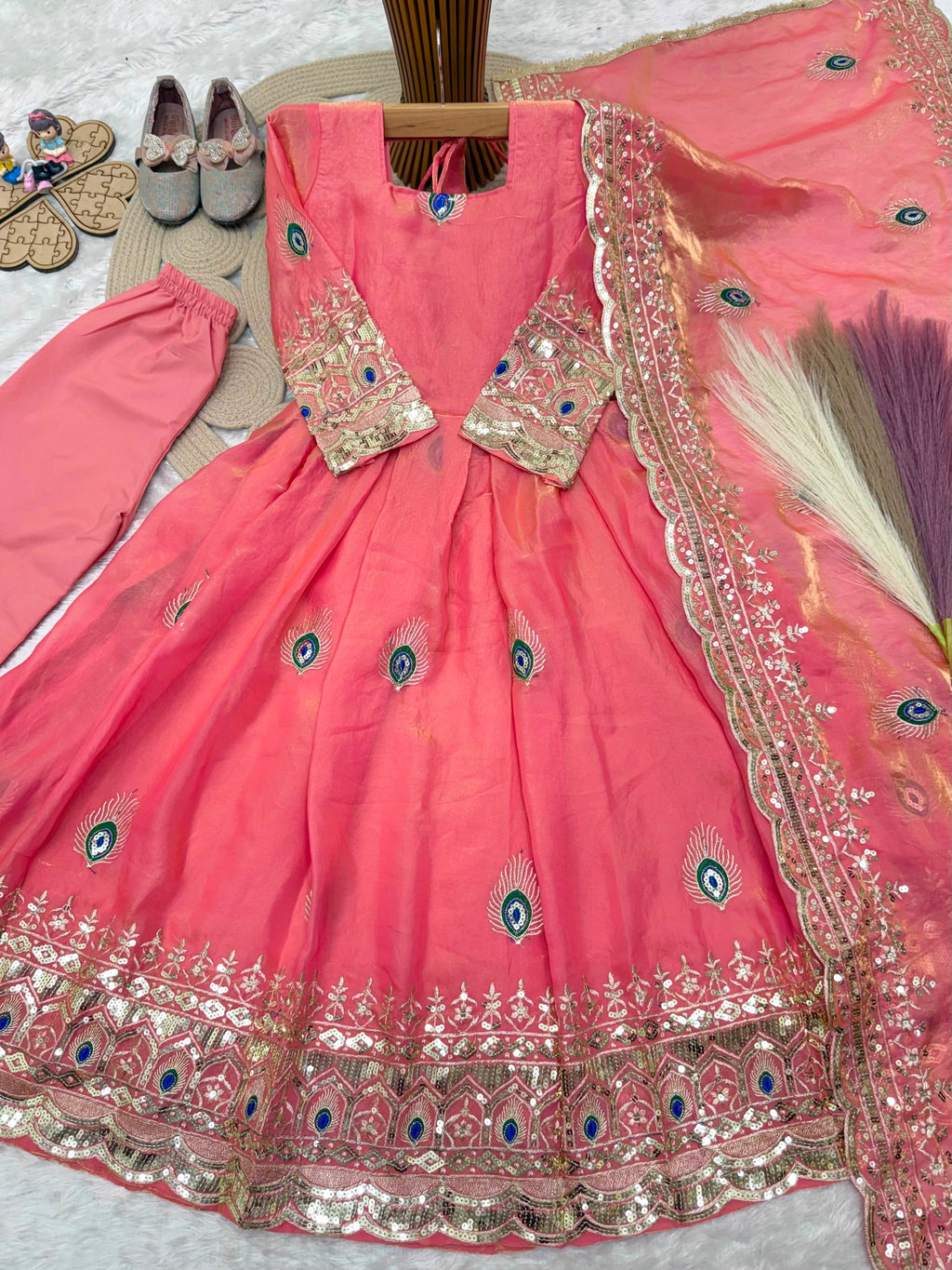 Coral pink ethnic kidswear girls anarkali set flat lay close view showing peacock feather and zari embroidery.