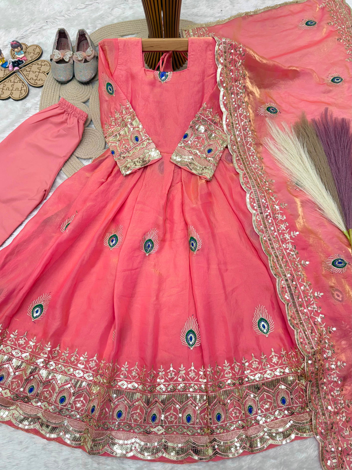 Coral pink ethnic kidswear girls anarkali set flat lay close view showing peacock feather and zari embroidery.